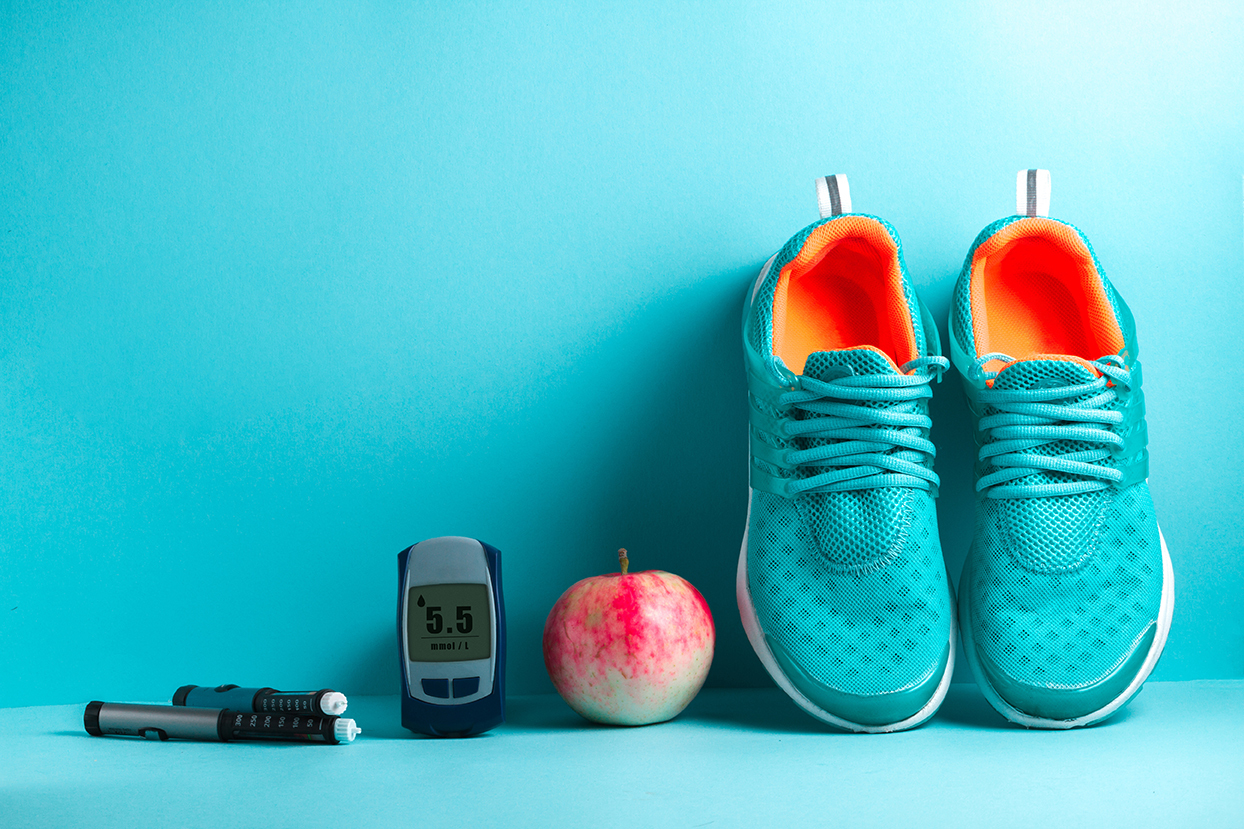 glucose monitor, insulin pens, an apple and sneakers, against a blue wall