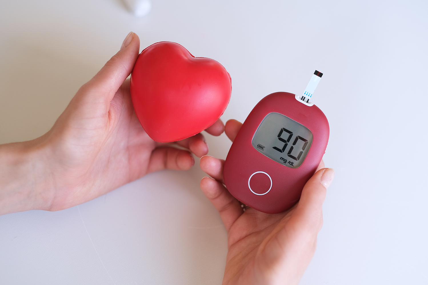 hands holding a rubber heart and a glucose monitor